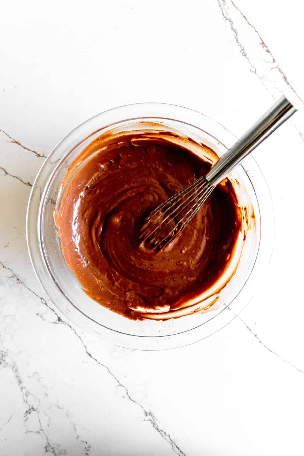 Chocolate and sweetened condensed milk mixed together in a glass bowl with a whisk.