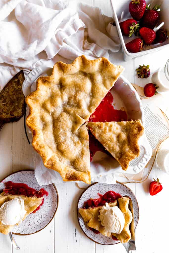 Strawberry rhubarb pie with slices missing and a dish of fresh strawberries.