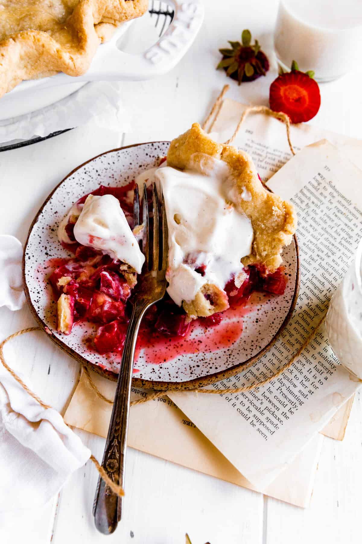Fork cutting into a slice of strawberry rhubarb pie topped with vanilla ice cream.