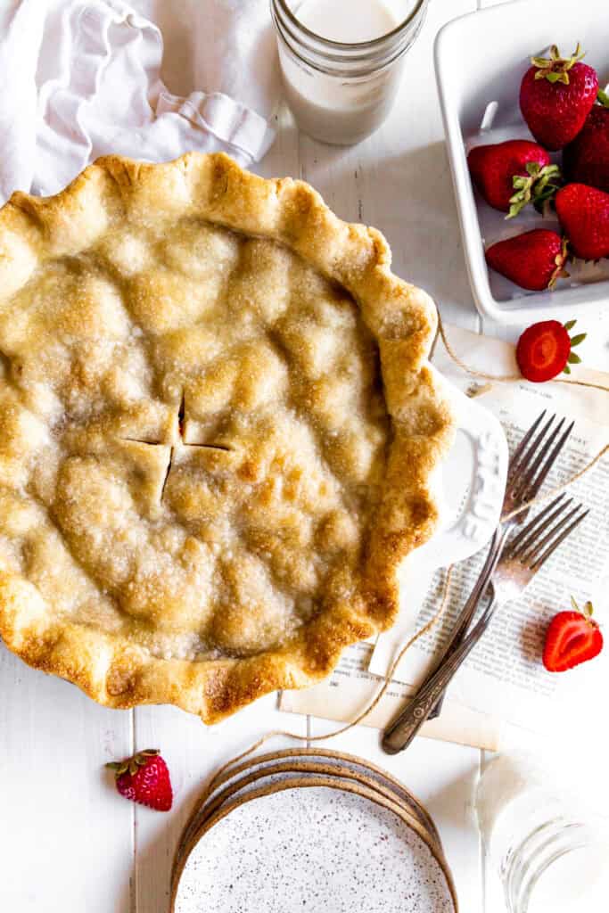 Strawberry rhubarb pie, a stack of plates and a carton of strawberries.