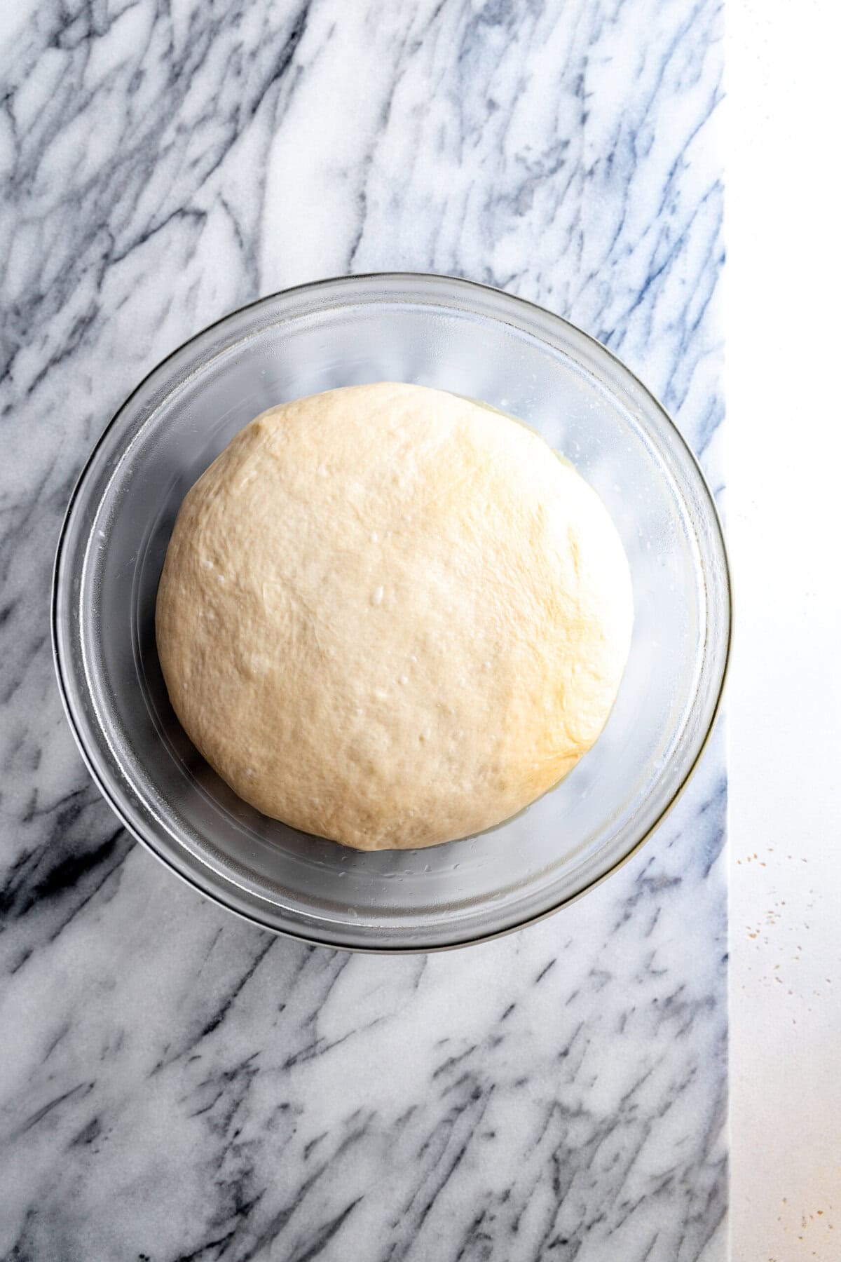 Proofed pizza dough in a glass bowl.