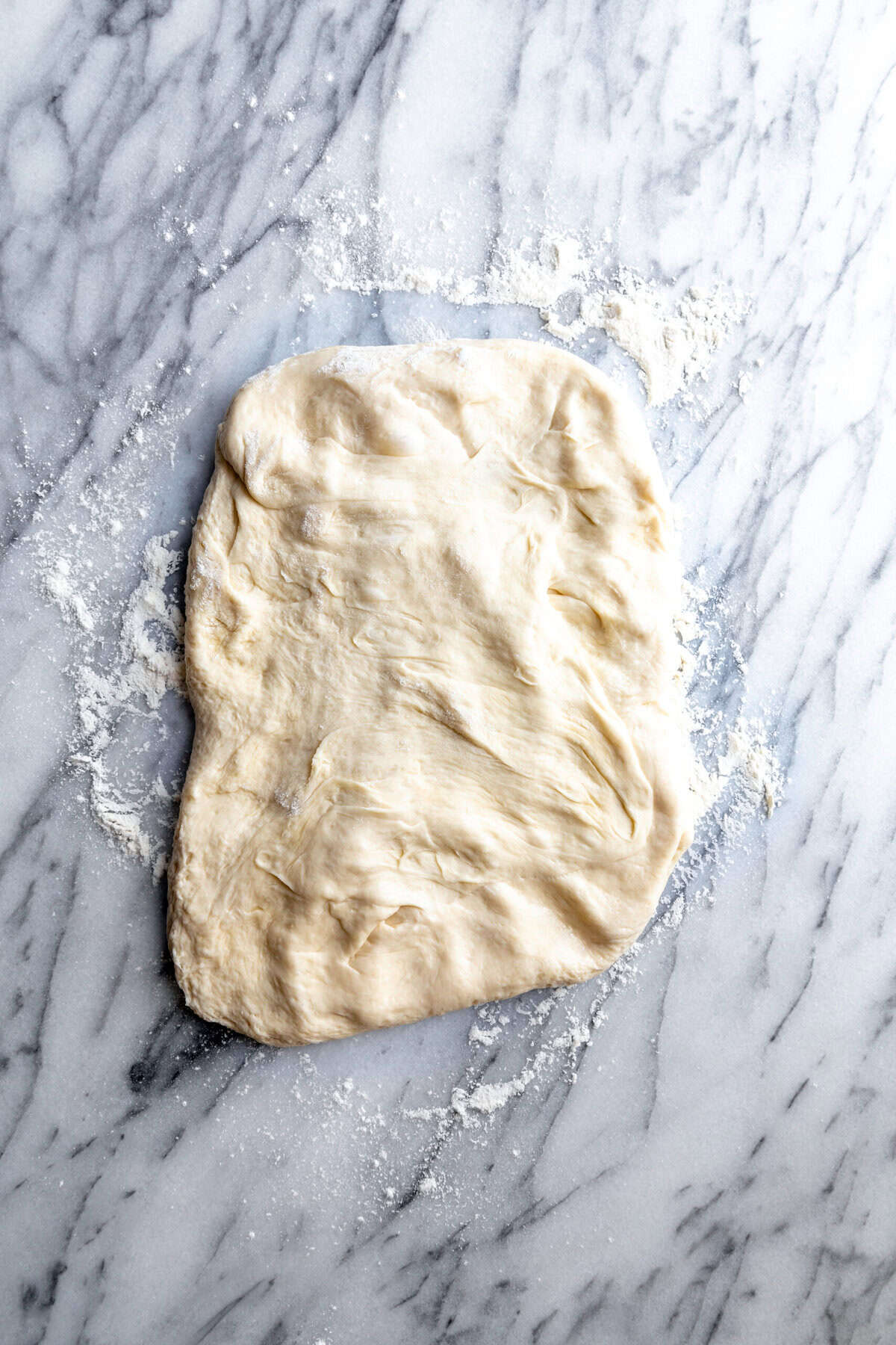 Pizza dough spread out on a marble surface.