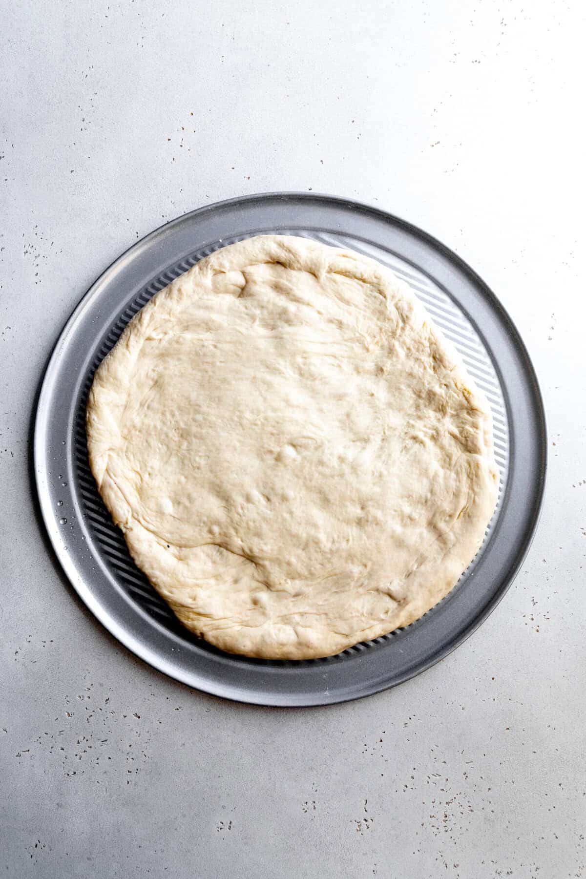 Pizza dough spread out on a pizza pan.
