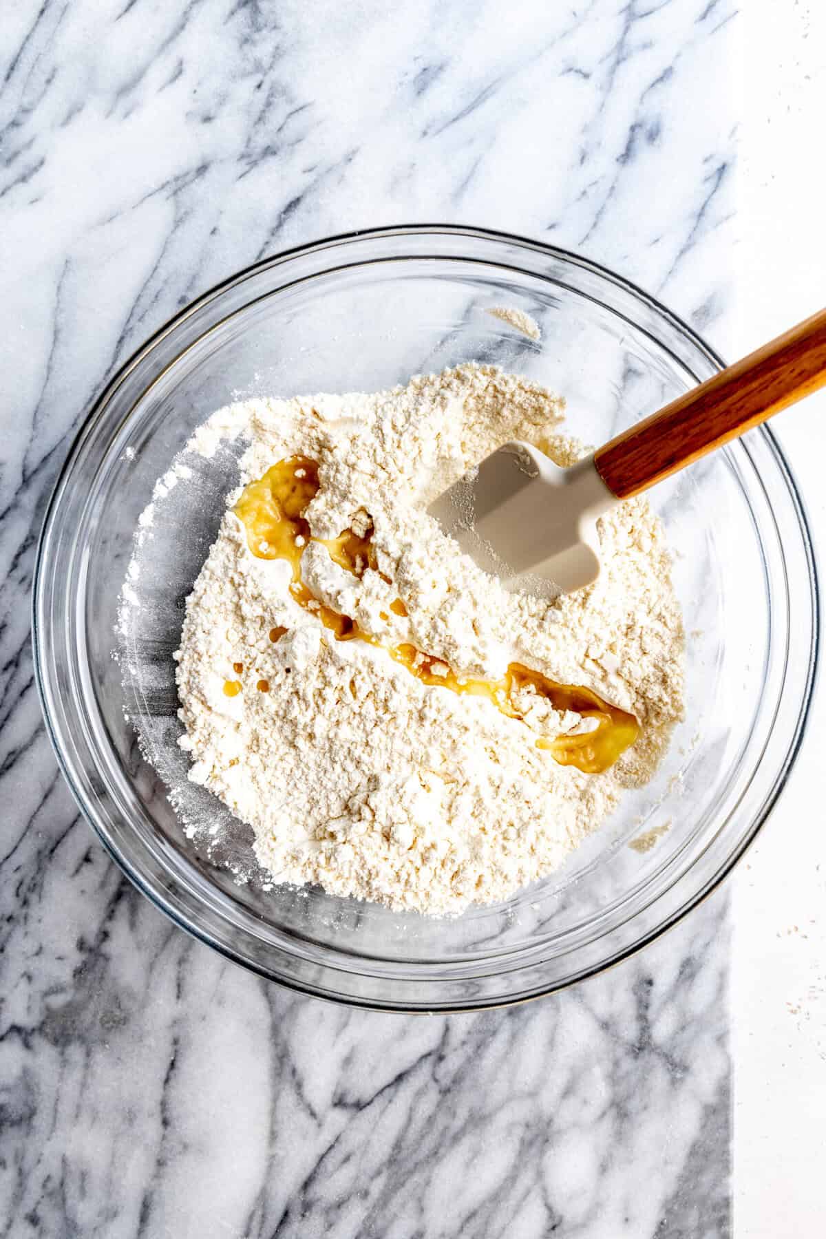 Olive oil drizzled over flour in a glass bowl with a rubber spatula.