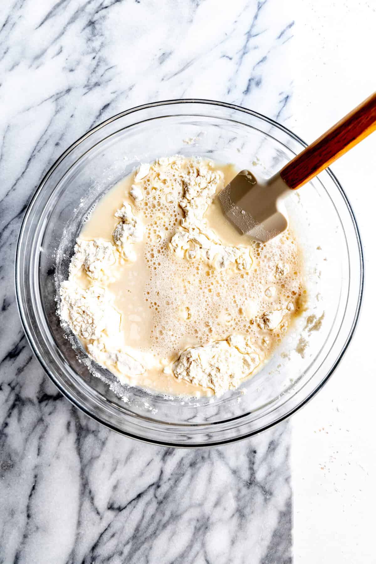 Water and flour in a glass bowl with a rubber spatula.