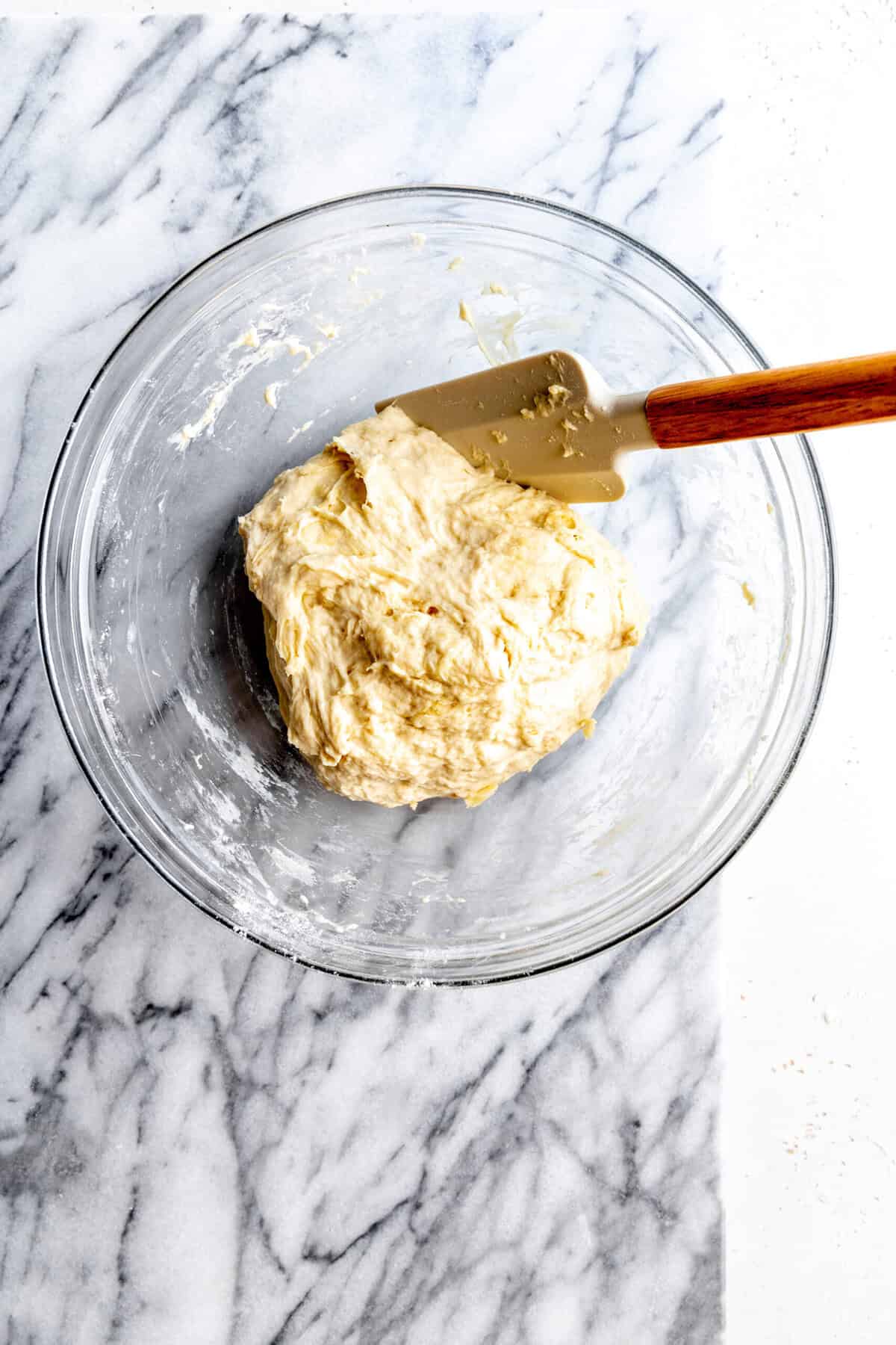 Pizza dough in a glass bowl with a rubber spatula.
