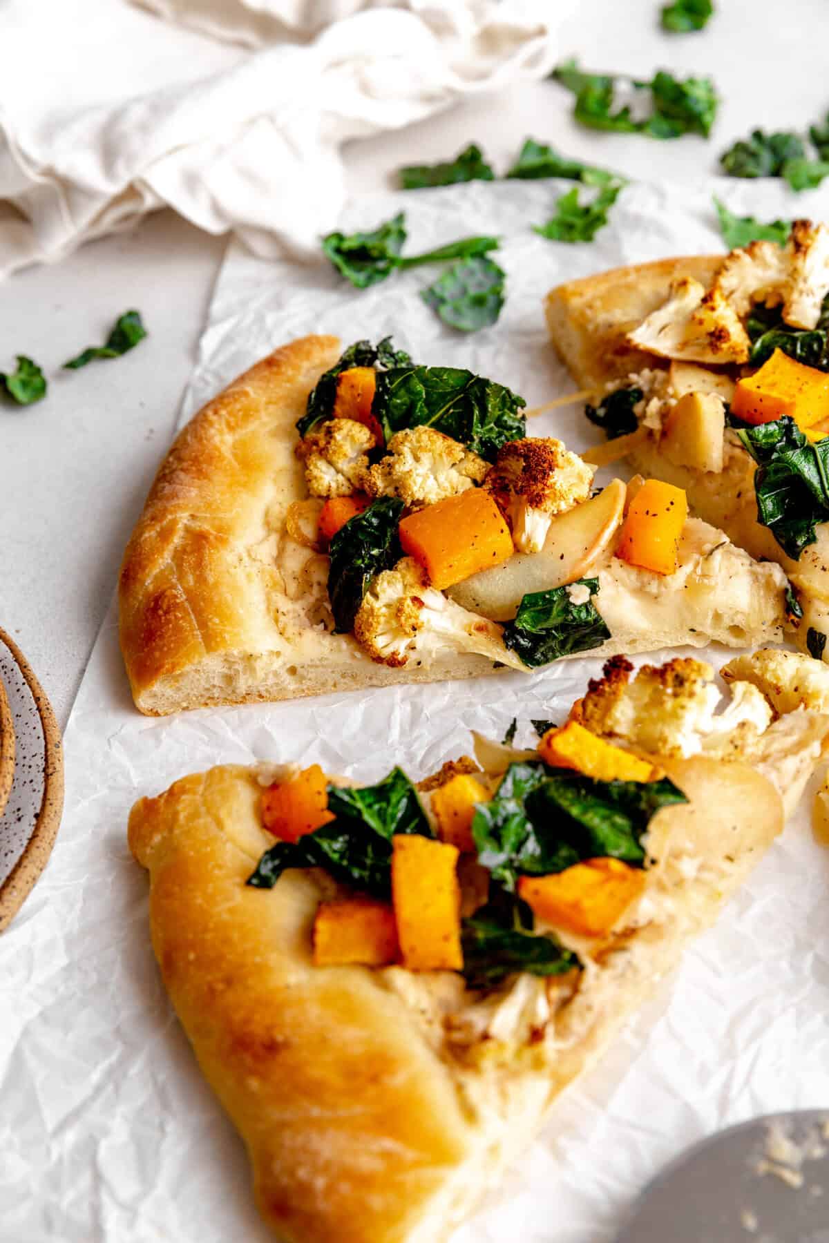 Slice of veggie pizza topped with cauliflower, butternut squash, apples and kale.