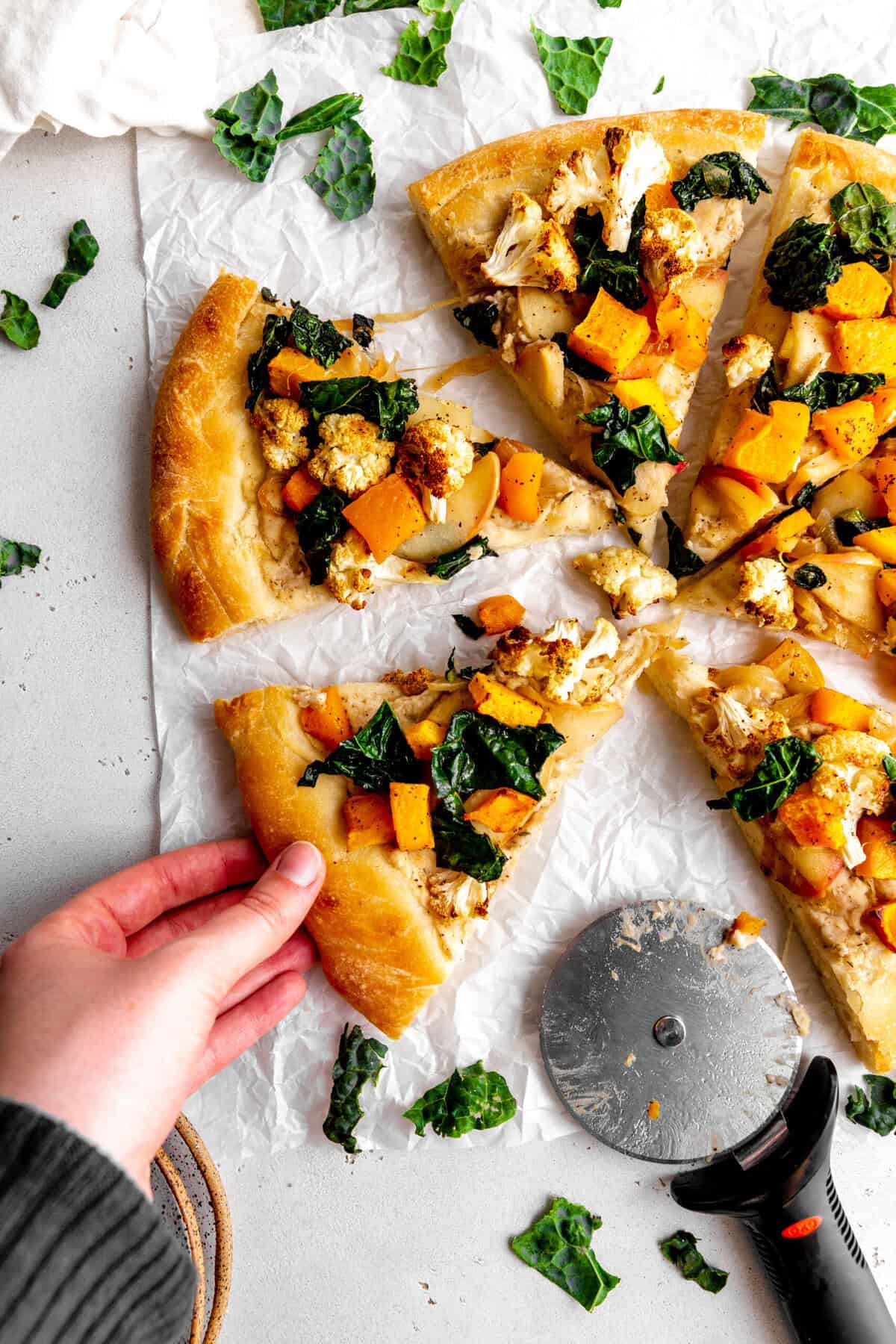 Hand grabbing a slice of roasted veggie pizza.