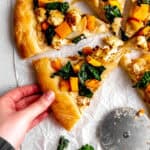 Hand grabbing a slice of roasted veggie pizza.