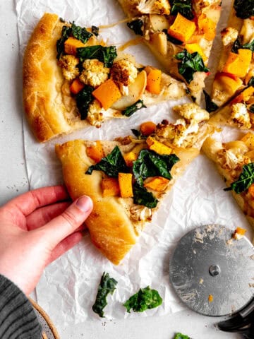 Hand grabbing a slice of roasted veggie pizza.