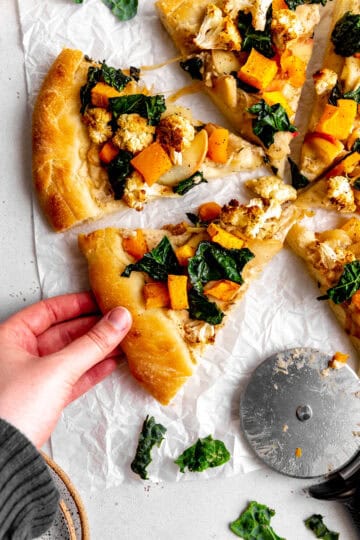 Hand grabbing a slice of roasted veggie pizza.