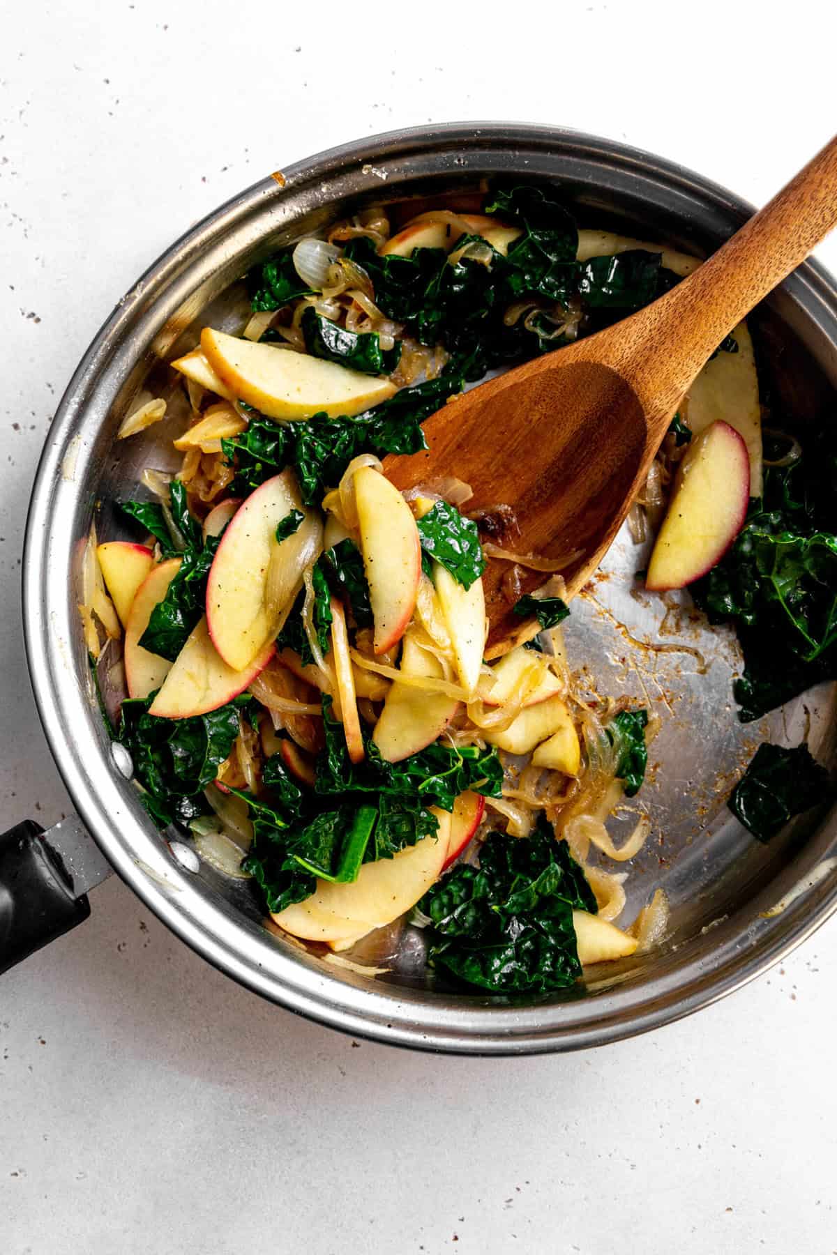 Sautéed onions, kale and apple slices in a skillet.