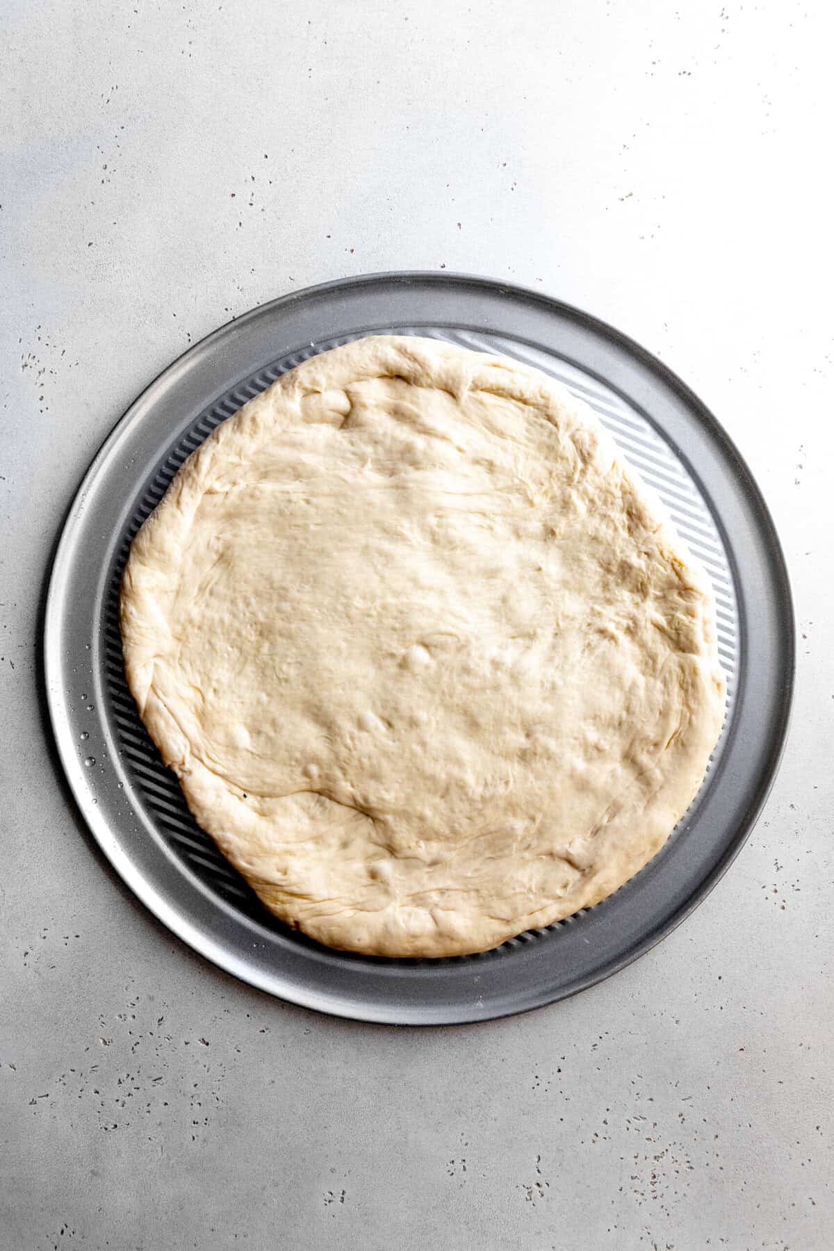 Pizza dough spread out on a pizza pan.