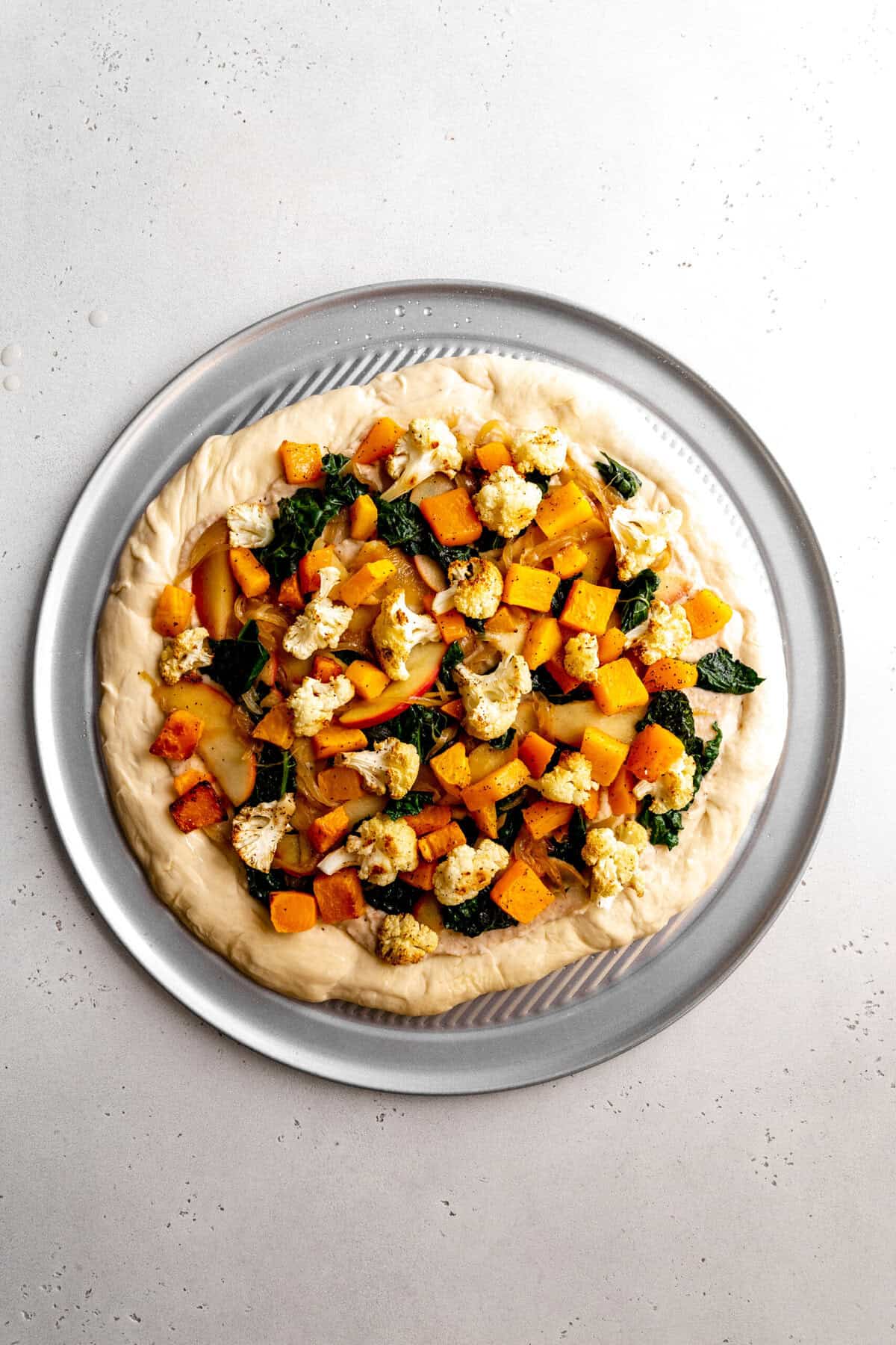 Unbaked roasted veggie pizza on a pizza pan.