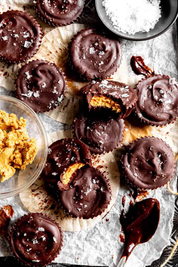 Chocolate peanut butter cups on a baking sheet and a bowl of flaky salt.