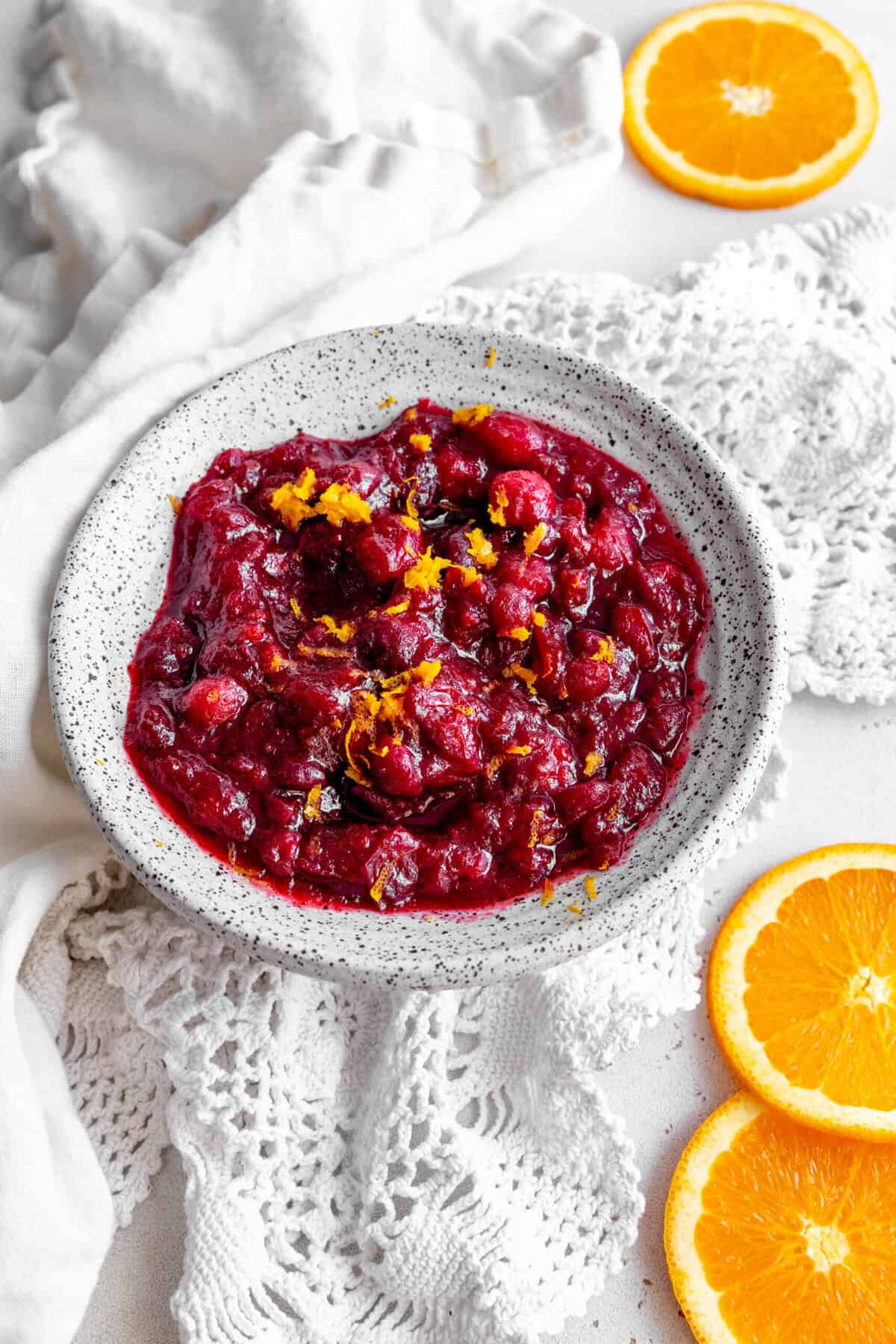 White bowl of cranberry sauce, linen napkin and orange slices.