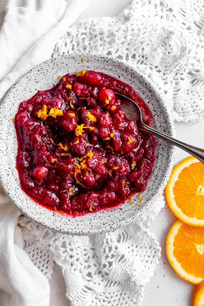 Spoon in a bowl of cranberry sauce and some orange slices.