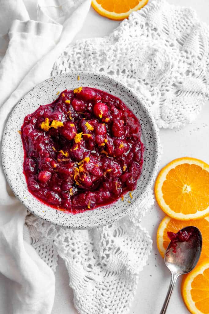 Bowl of cranberry sauce, orange slices and a silver spoon.