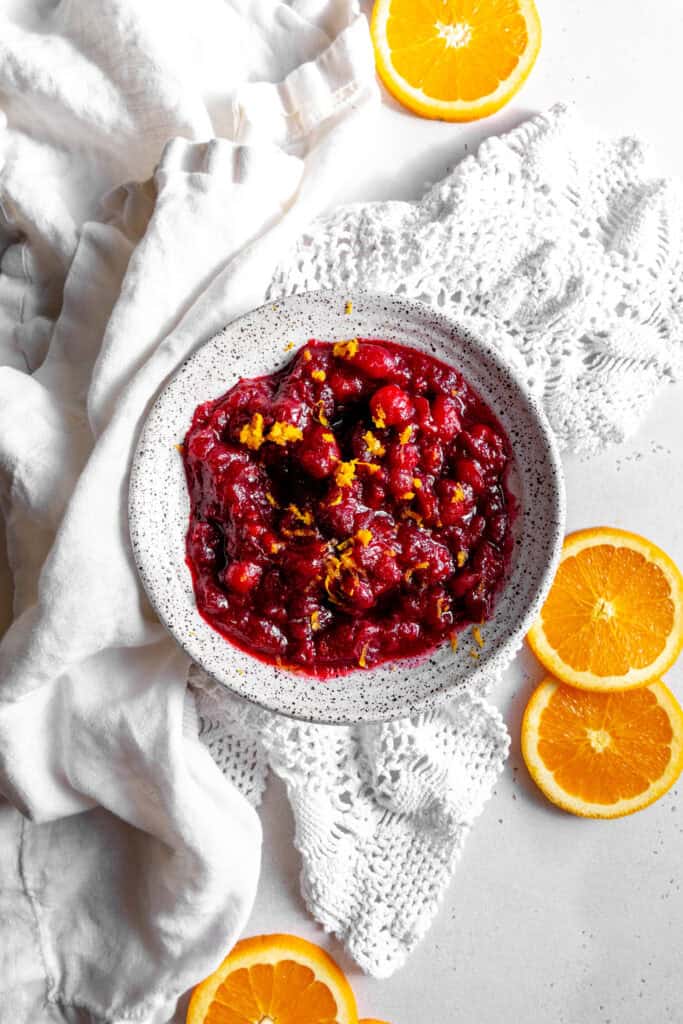 White bowl of cranberry sauce, linen napkin and orange slices.