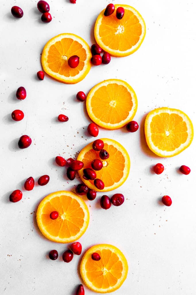 Orange slices and fresh cranberries on a white surface.