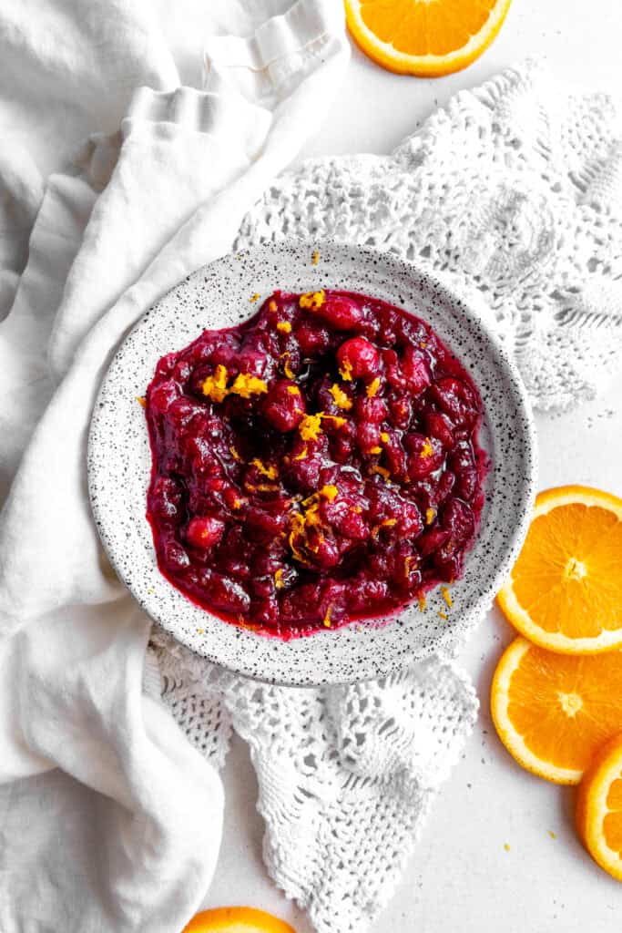 White bowl of cranberry sauce, linen napkin and orange slices.
