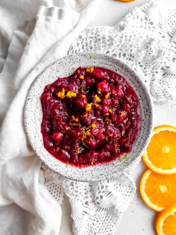White bowl of cranberry sauce, linen napkin and orange slices.