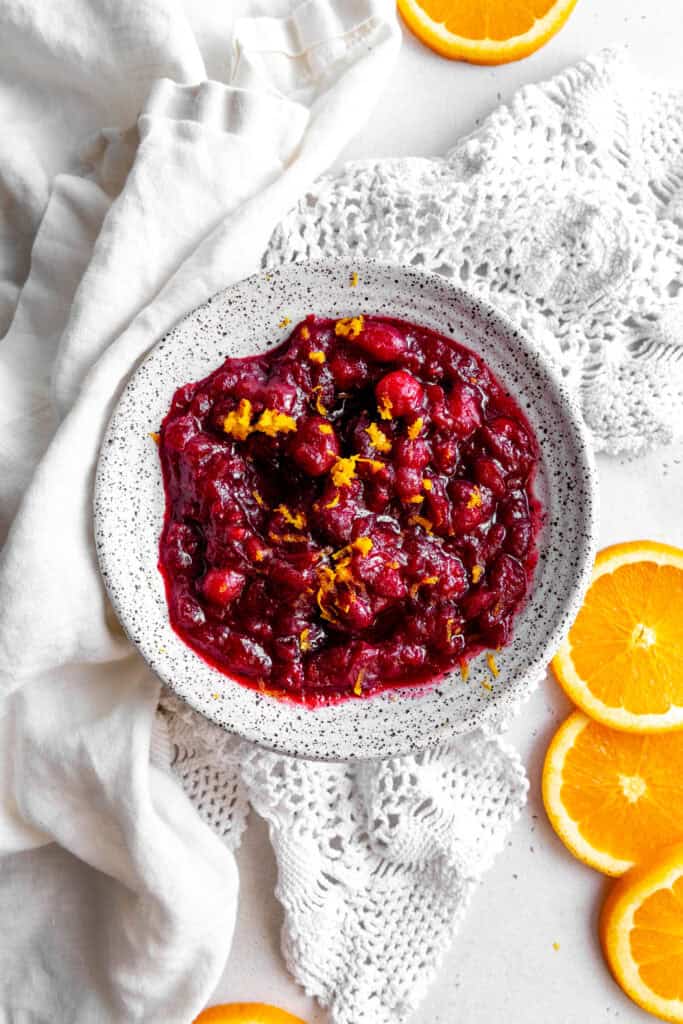 White bowl of cranberry sauce, linen napkin and orange slices.