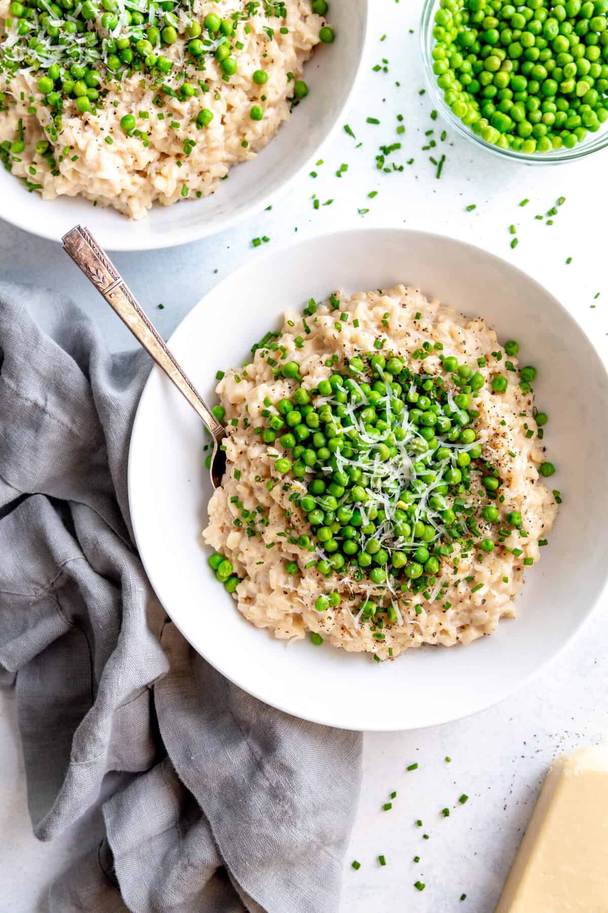 Two bowls of risotto, a small bowl of peas and a block of parmesan cheese.