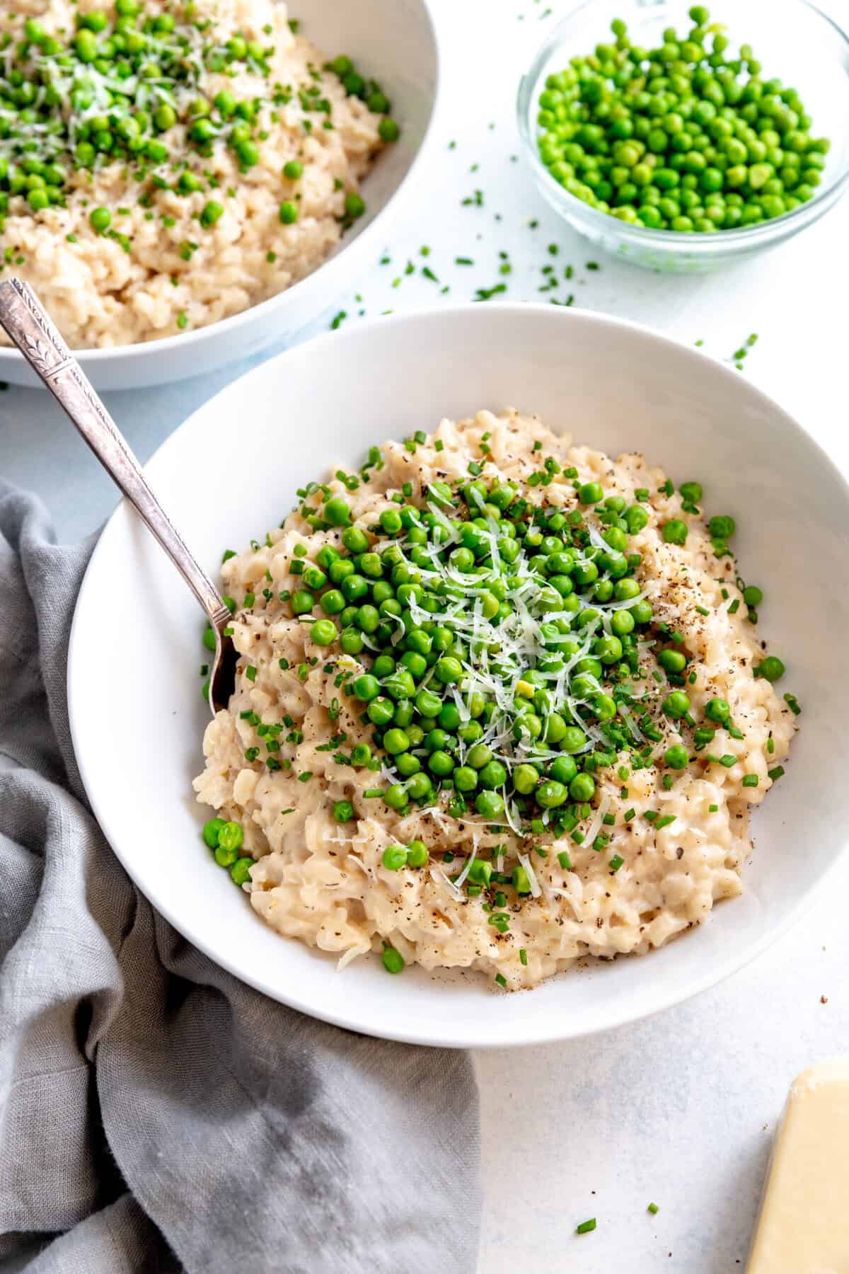 Spoon sticking in a bowl of risotto topped with green peas.
