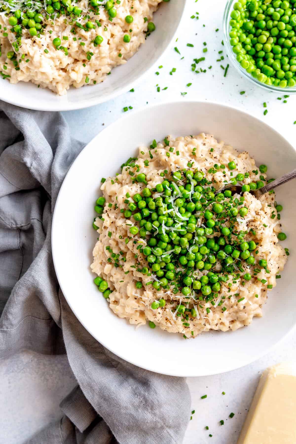 Two bowls of risotto, a small bowl of peas and a block of parmesan cheese.
