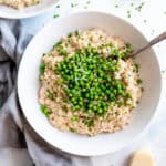 Spoon digging into a bowl of risotto topped with green peas and parmesan.