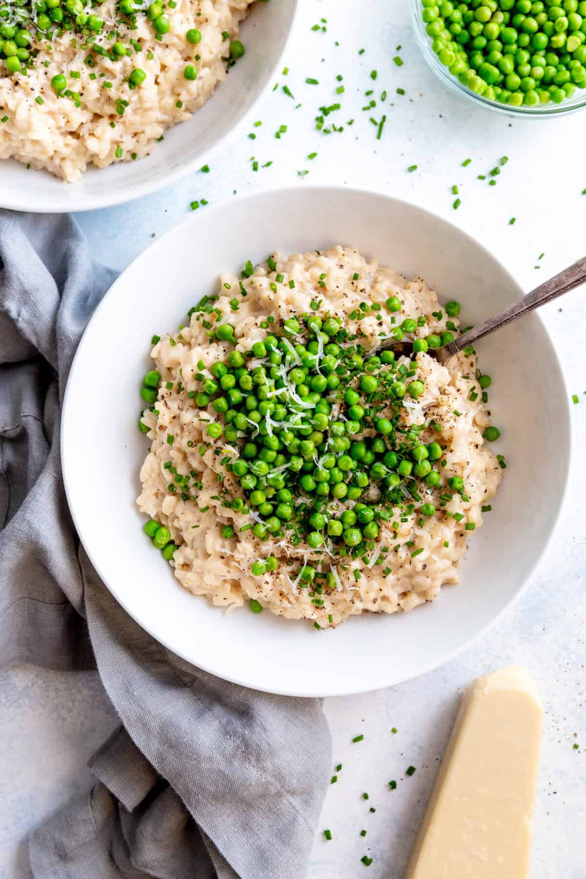 Spoon digging into a bowl of risotto topped with green peas and parmesan.