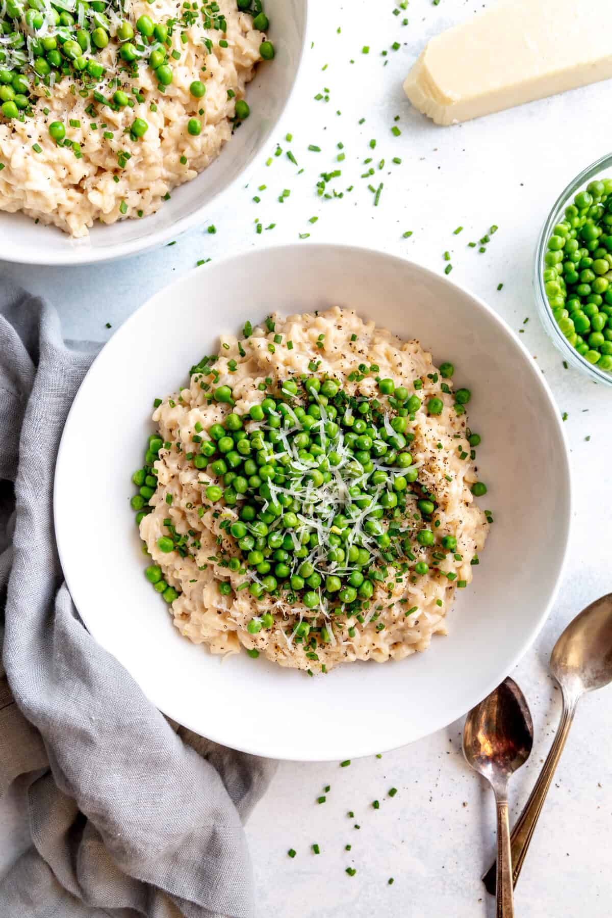 Bowl of garlic white wine risotto topped with green peas, a gray napkin and a block of parmesan.