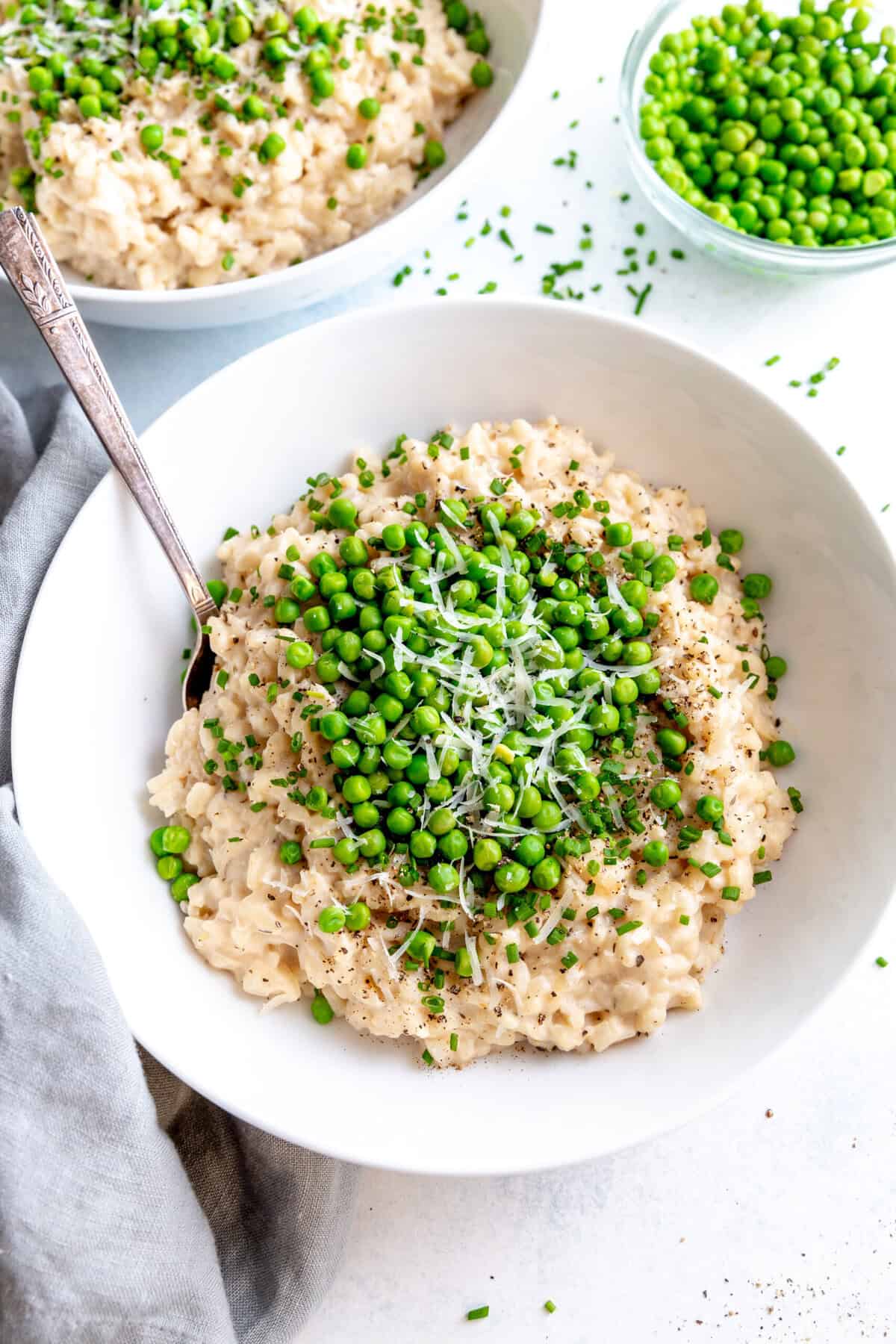 Spoon digging into a bowl of garlic white wine risotto topped with green peas and chives.