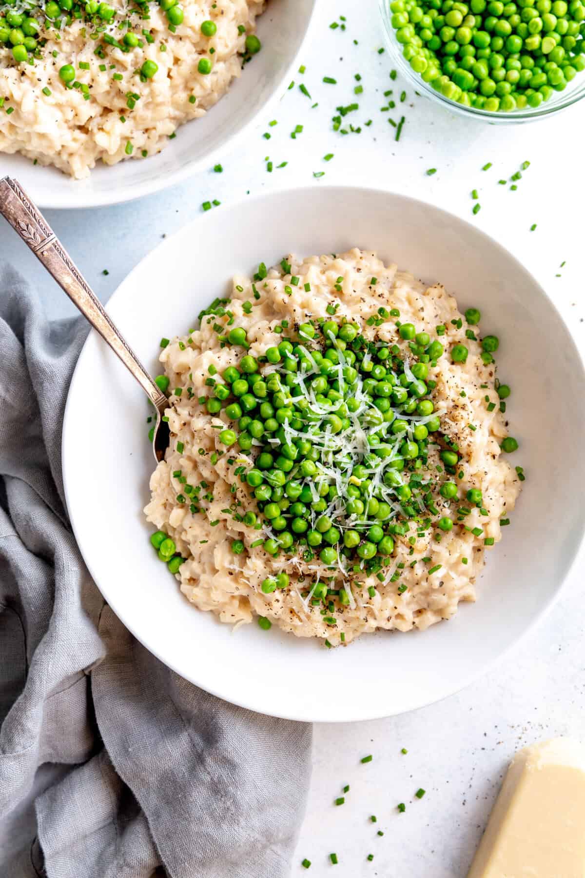 Two bowls of garlic white wine risotto, a small bowl of peas and a block of parmesan cheese.