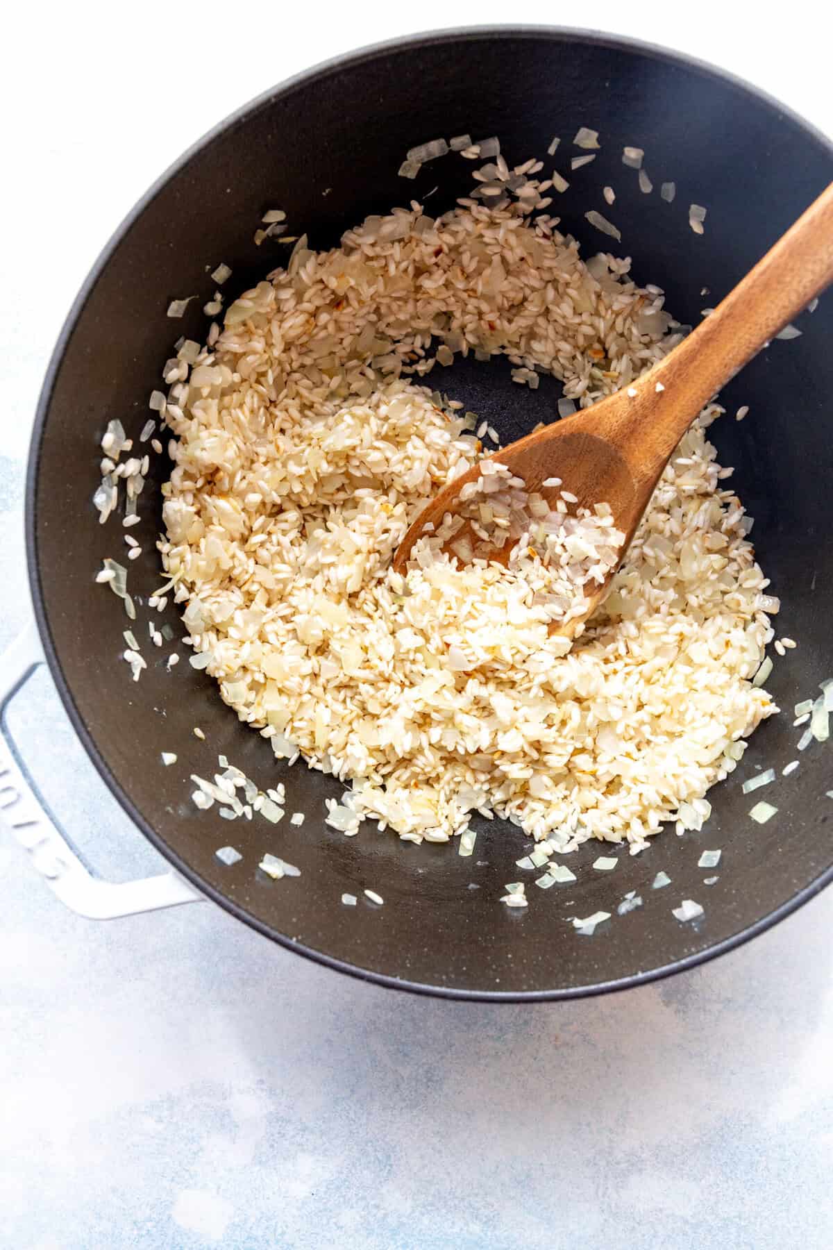 Wooden spoon stirring sautéed rice in a pot.