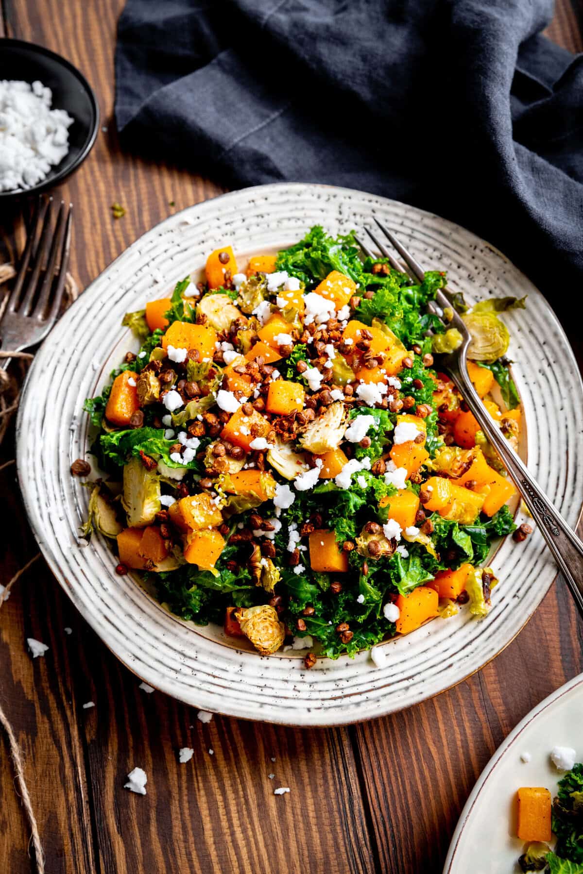 Fork digging into a plate of kale salad with butternut squash.