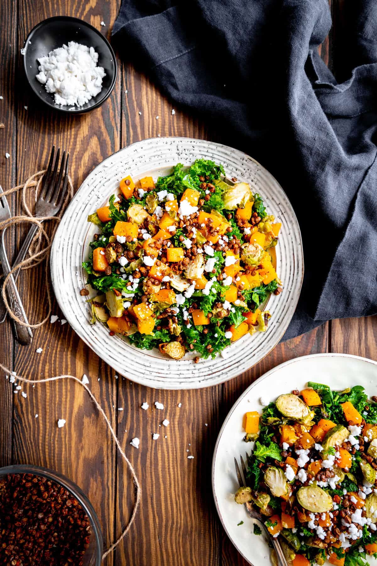 Two plates of kale butternut squash salad, a bowl of crispy lentils and a napkin.