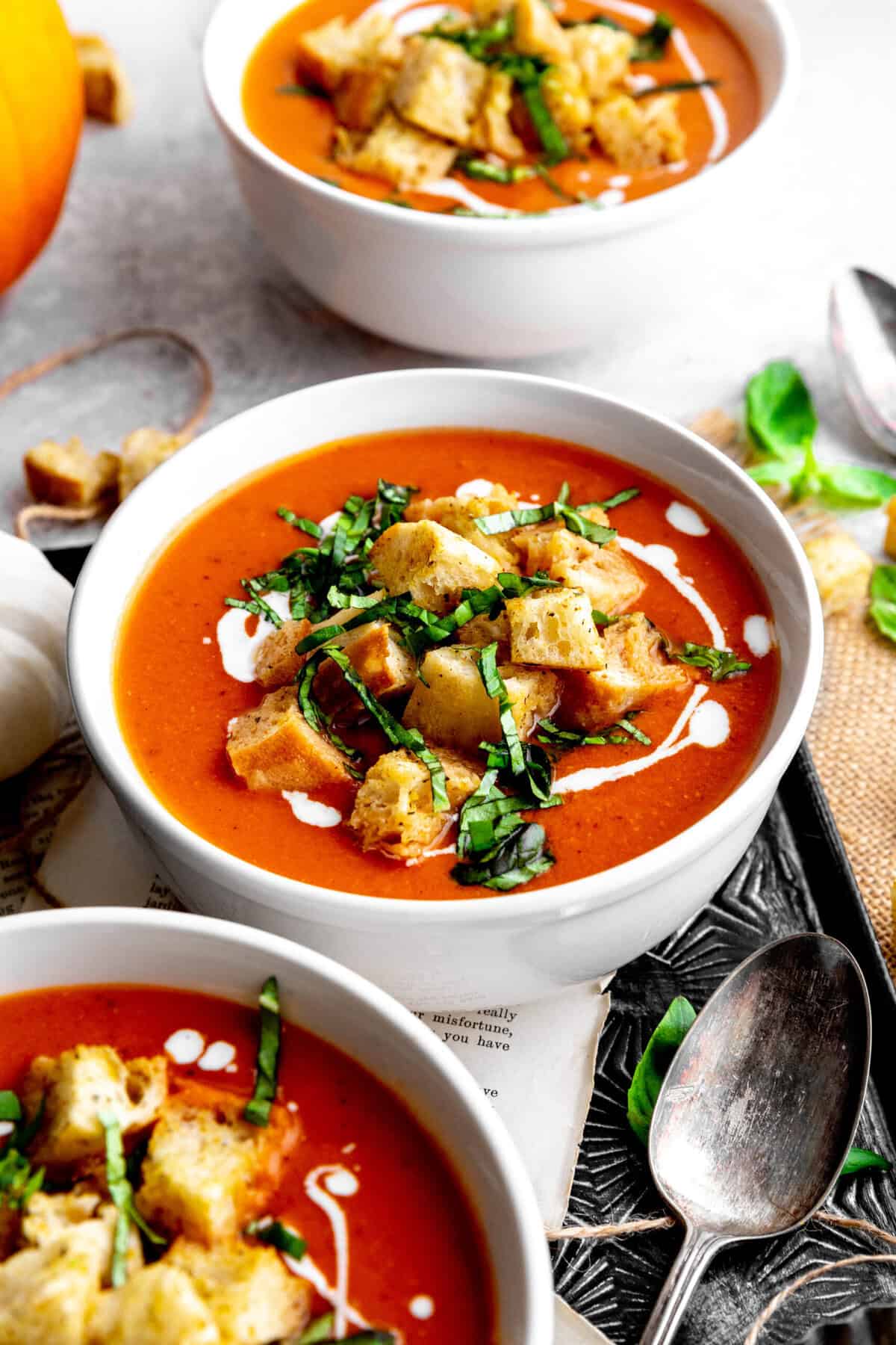 Three bowls of pumpkin tomato soup on a tray with spoons.