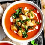 Bowl of pumpkin tomato soup topped with croutons and fresh basil.