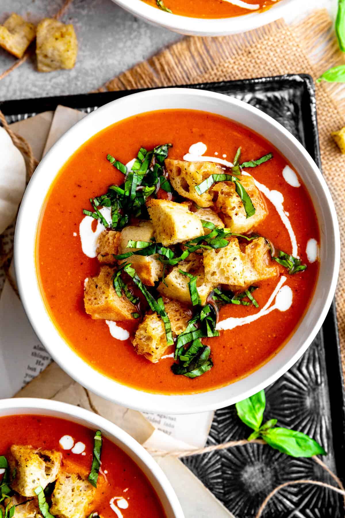 Bowl of pumpkin tomato soup topped with croutons and fresh basil.