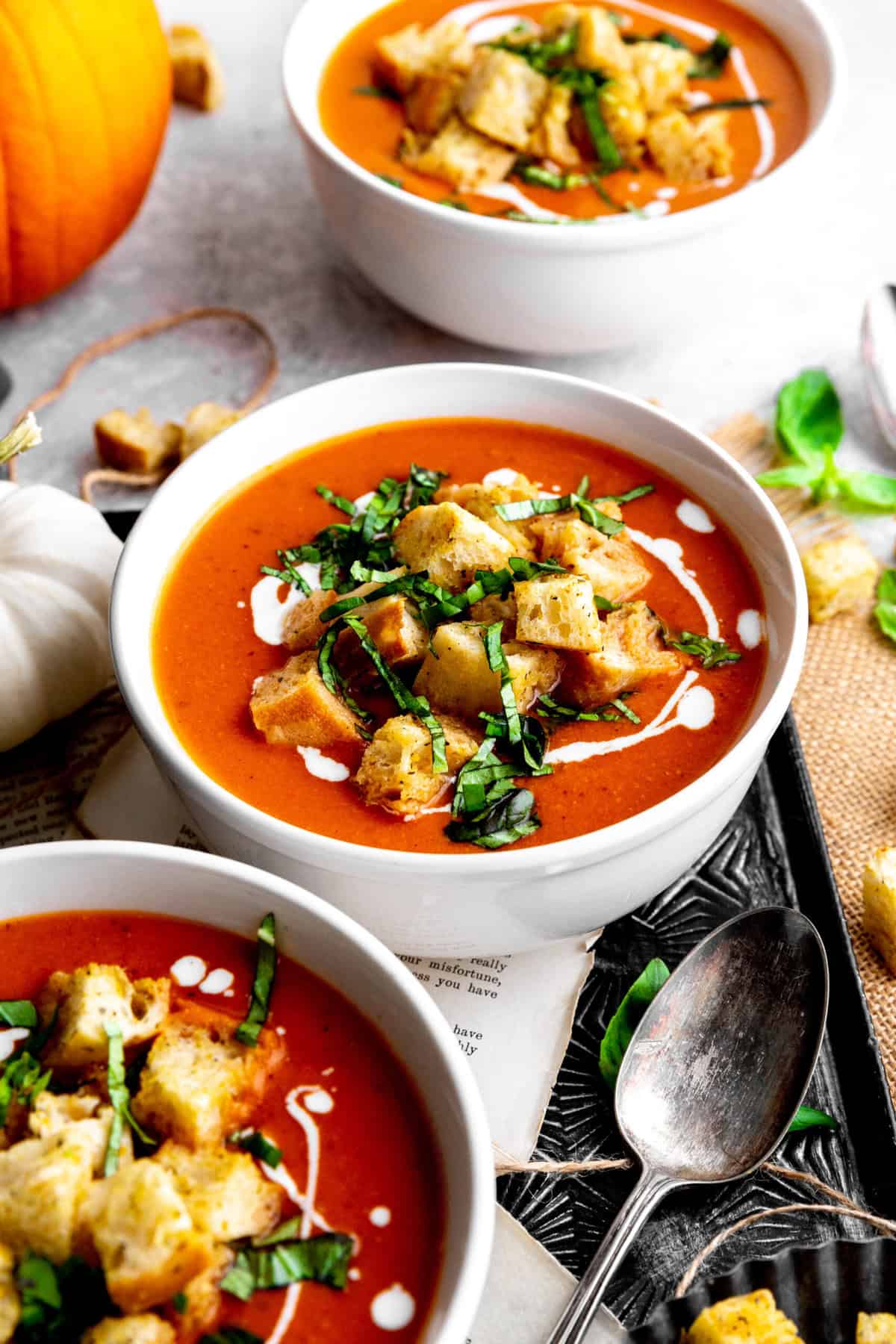 Three bowls of pumpkin tomato soup on a tray with a pumpkin.