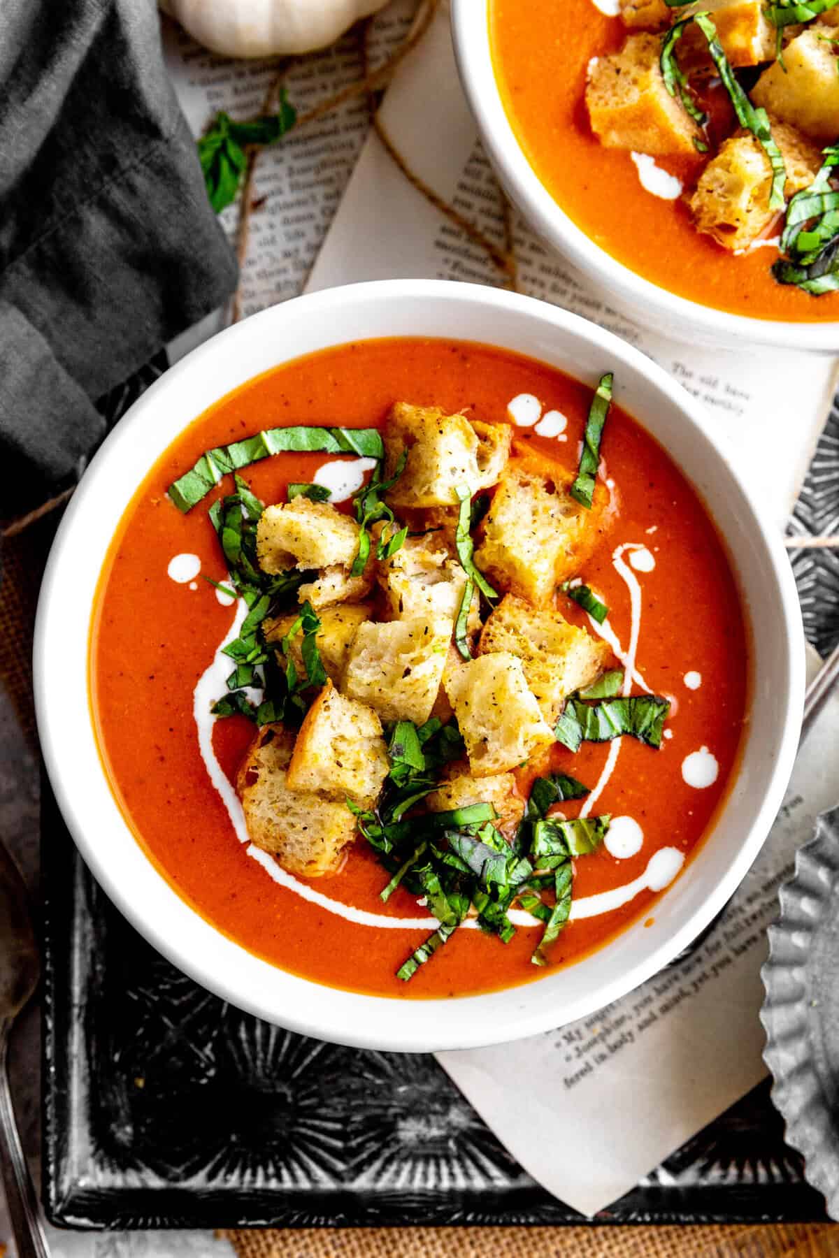 Bowl of pumpkin tomato soup topped with croutons and fresh basil.