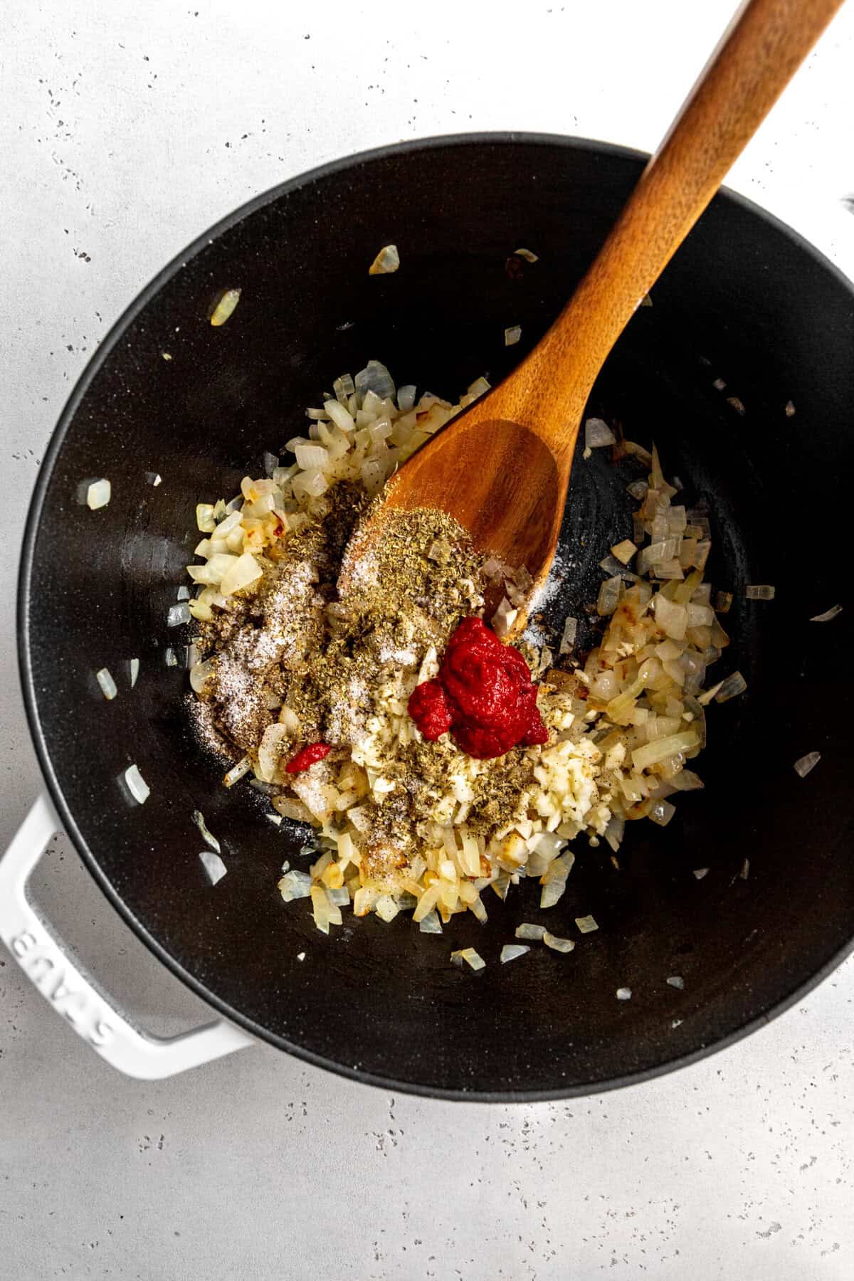 Sautéed onions, tomato paste and spices in a pot with a wooden spoon.