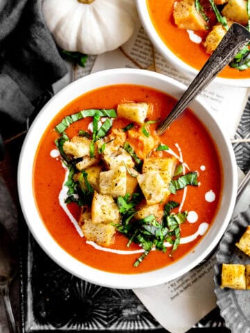 Bowl of pumpkin tomato soup on a tray with a white pumpkin.