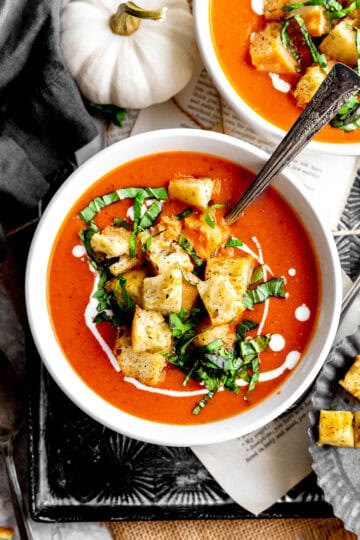 Bowl of pumpkin tomato soup on a tray with a white pumpkin.