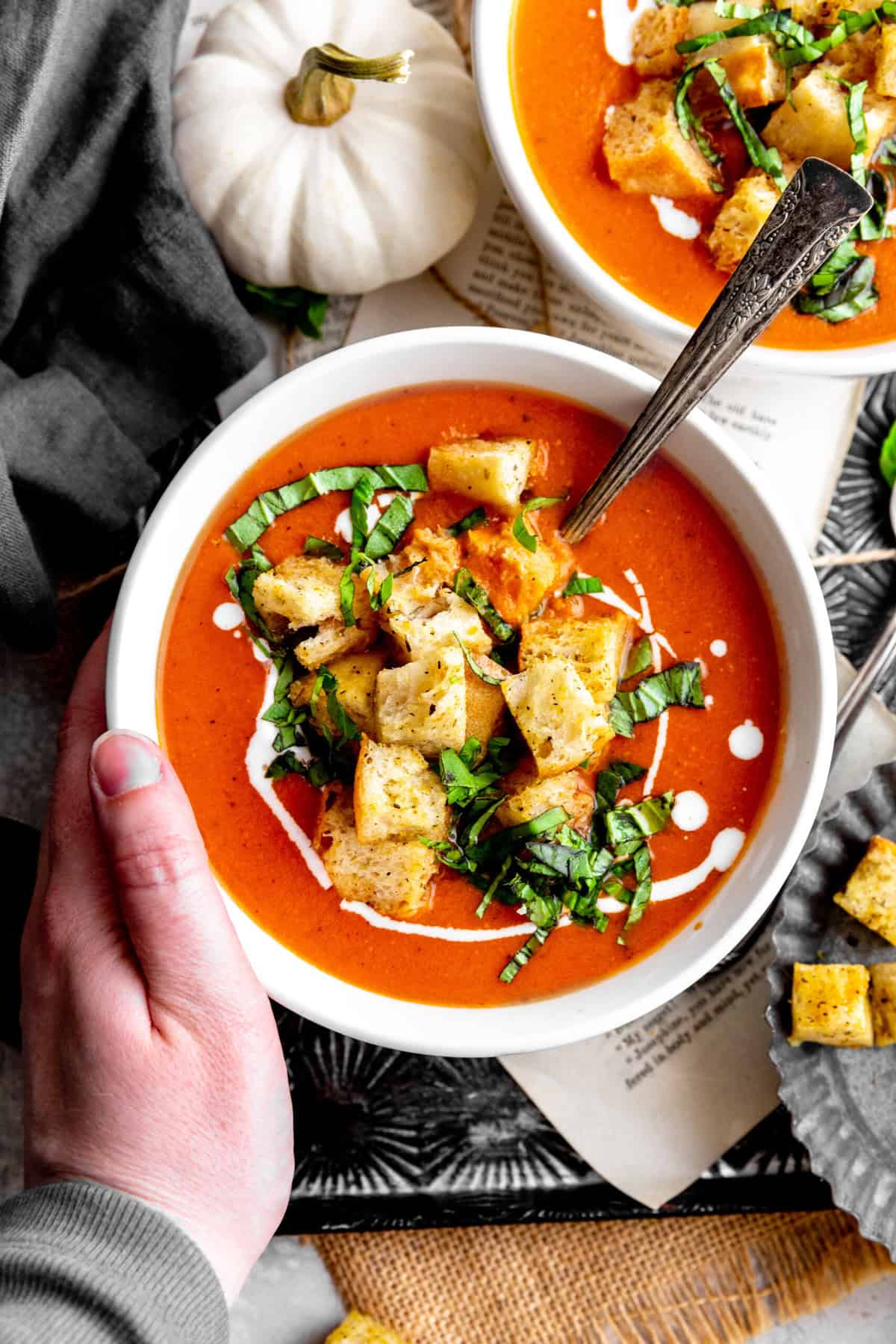 Hand resting on a bowl of pumpkin tomato soup.