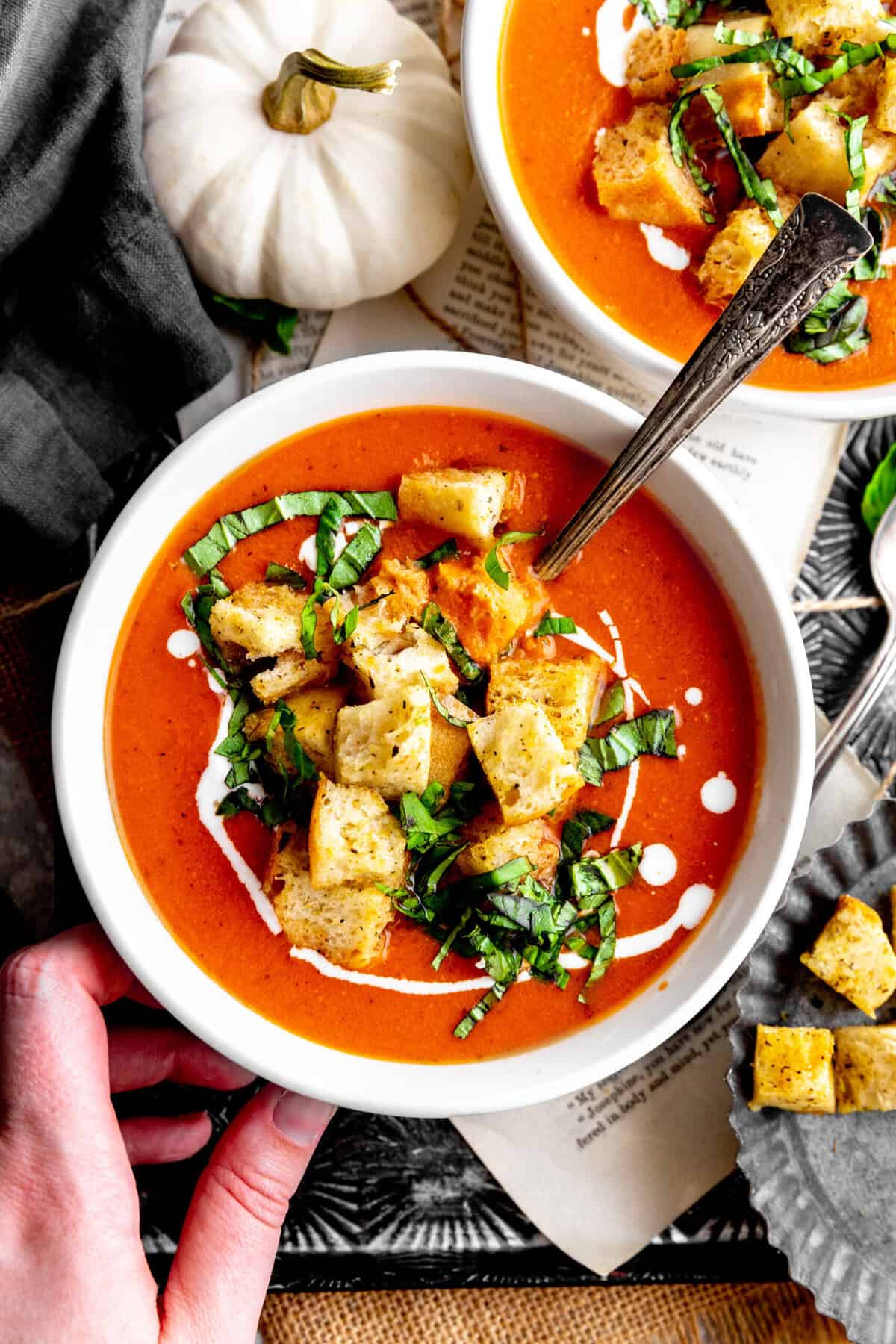Hand resting on a bowl of pumpkin tomato soup.