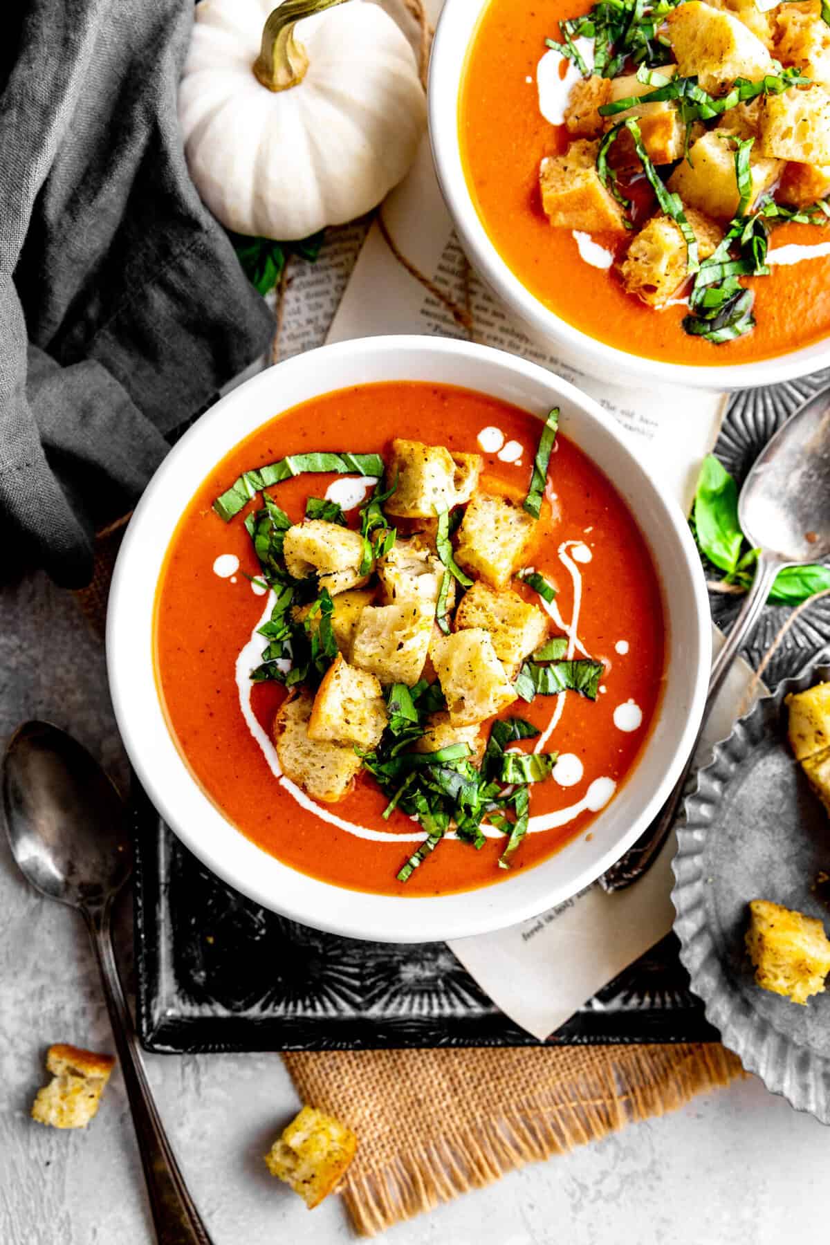 Two bowls of pumpkin tomato soup on a tray with a pumpkin and croutons.