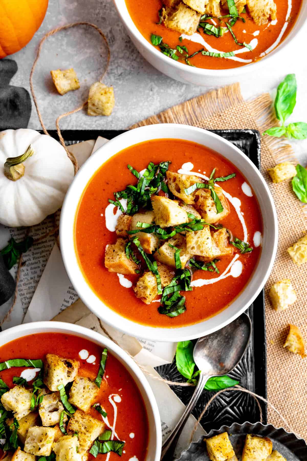 Three bowls of pumpkin tomato soup on a tray with spoons and croutons.